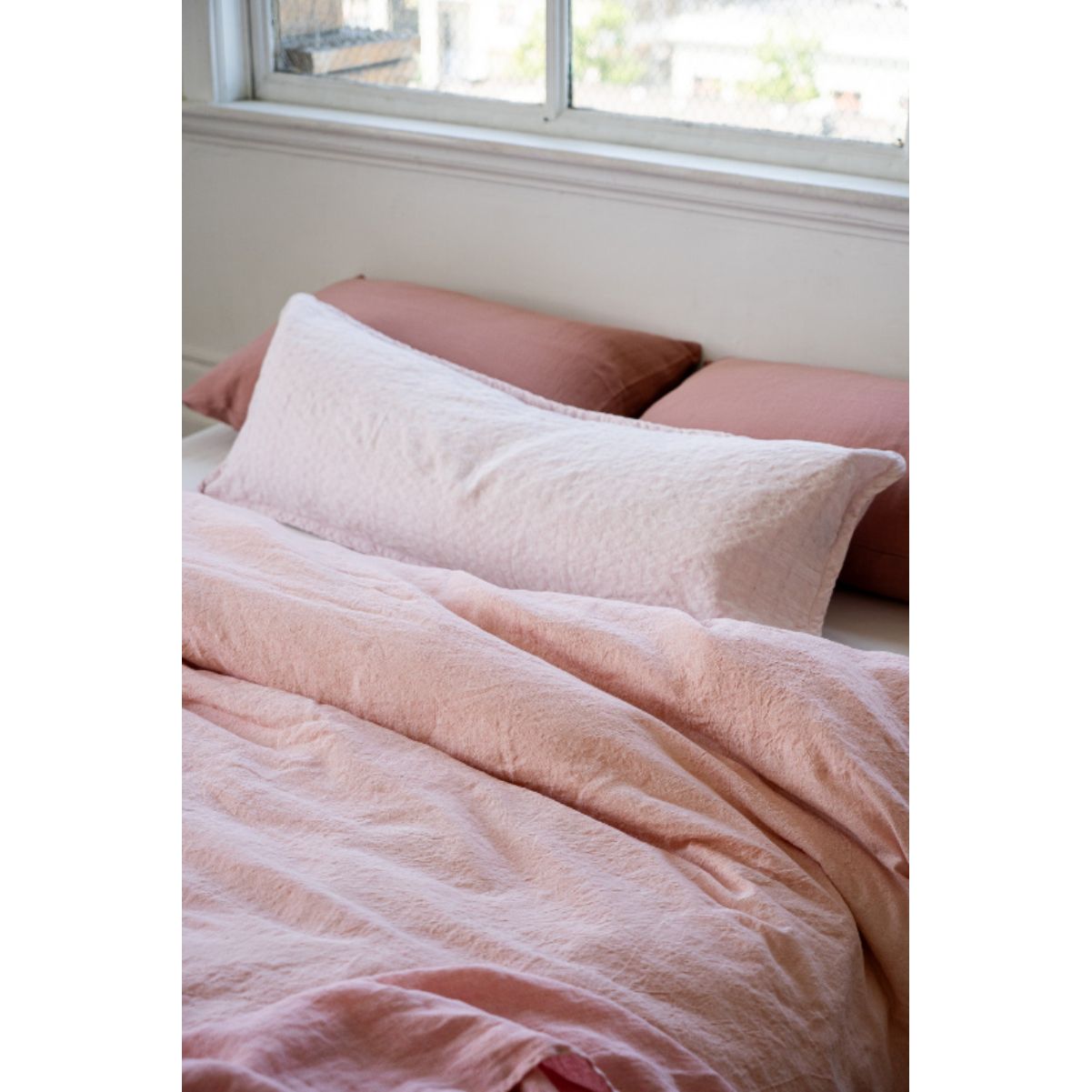 Pink textured duvet and pillows on a bed with a window in the background