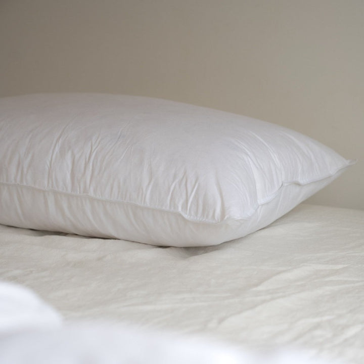A close up of a white Somn Home luxury duck feather pillow insert cushion insert on a bed.